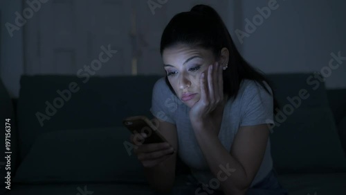 young attractive and tired hispanic 30s woman with mobile phone looking serious and bored using dating app sitting at apartment living room couch late night