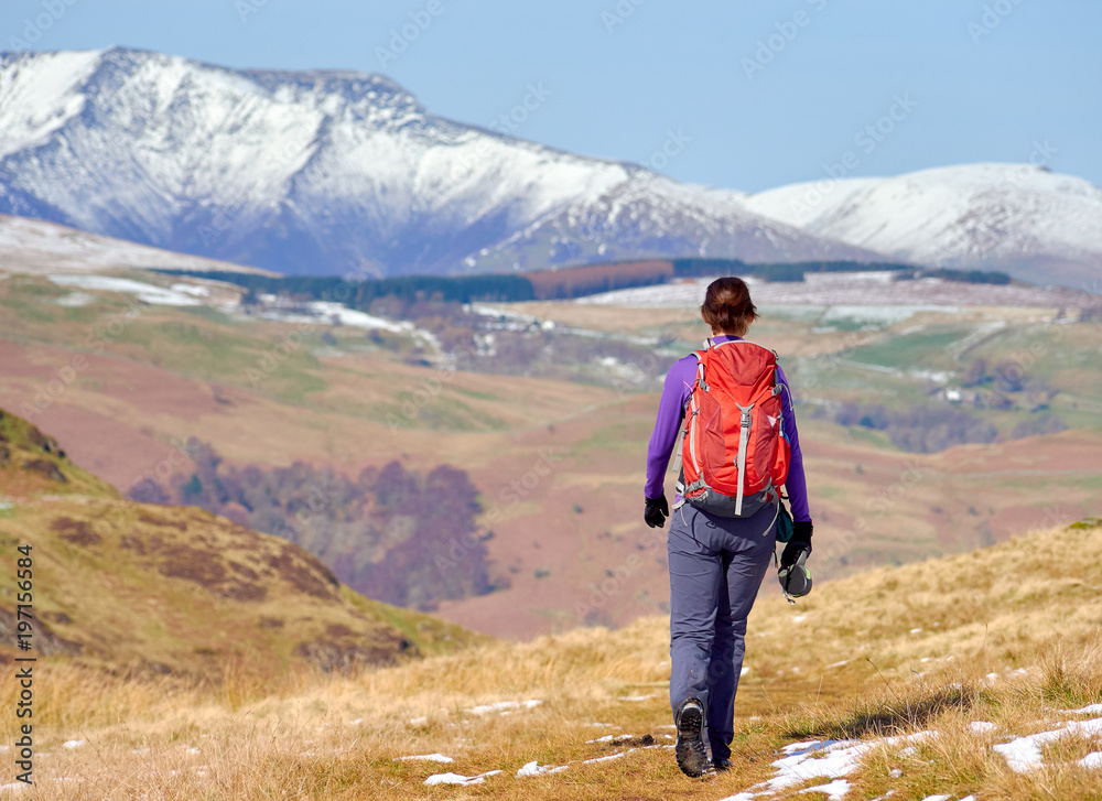 A female hiker descending from a snow covered Place Fell summit with Blenccathra in the English Lake District.