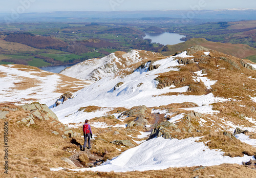 A female hiker descending from a snow covered Place Fell and the Knight summit in the English Lake District.