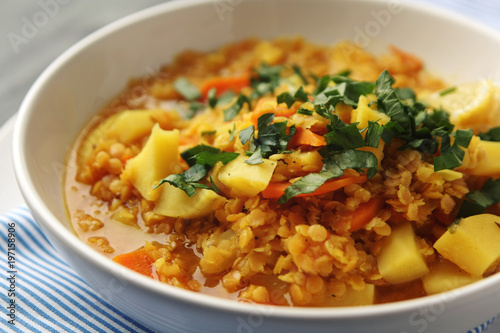 Red lentil stew with potato, carrot and turmeric. Toned photo. Healthy lunch on the round white plate. Colorful vegan dish with potato, carrot and turmeric. European cuisine. Vegetarian.