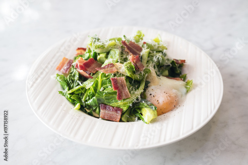 Closeup image of warm salad with bacon and egg in white plate in the restaurant