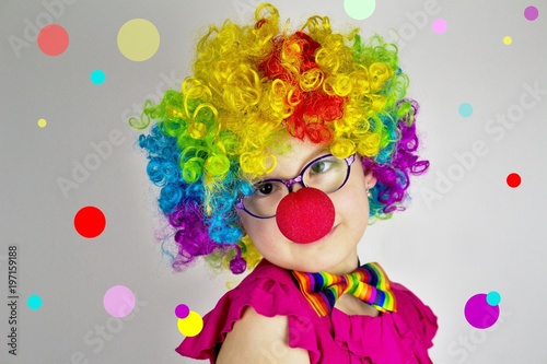 Little girl in clown costume in front of  background with colorful dots.Little girl with glasses in colorful clown costume.