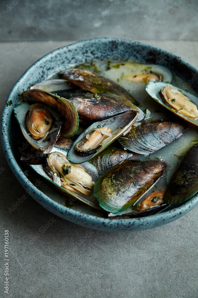 Kiwi mussels cooked in marinier sauce with white wine and parsley in hand-crafted blue ceramic plate on gray background
