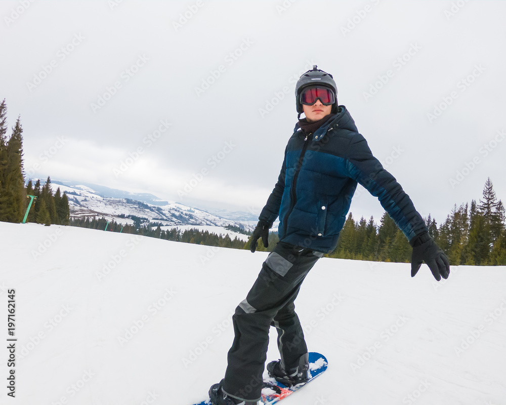A young man in sports glasses and in the helmet is riding a snowboard in the mountains in Transcarpathia.