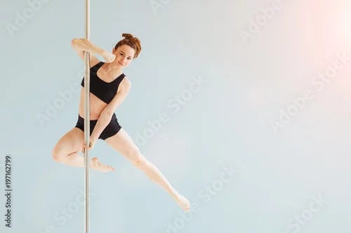 Obraz Piękna tancerka na rurze w studio. Seria zdjęć kobiety w średnim wieku rudych włosów w czarnym biustonoszu i szortach do ćwiczeń tańca na rurze w różnych pozach. Szare tło.