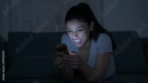 young attractive and relaxed hispanic 30s woman with mobile phone smiling happy using dating app late night in internet social media addiction concept
