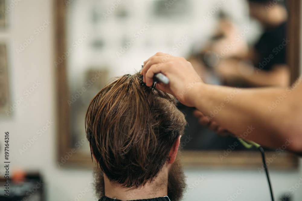 Master cuts hair and beard of men in the barbershop and uses a hair dryer Master cuts hair and beard of men in the barbershop and uses a hair dryer