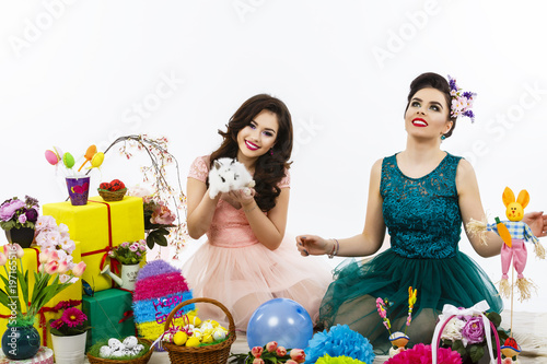 Two beautiful women playing in easter decoration with a rabbit. makeup and special hairstyle for holidays
