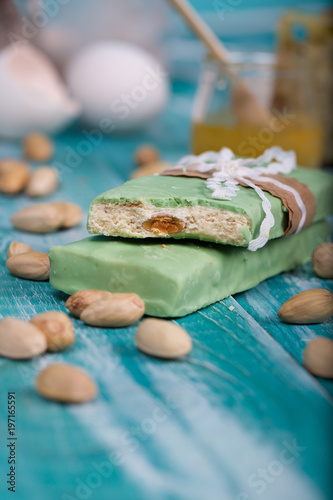 Almond turron covered by pistachio chocolate on a wooden surface.