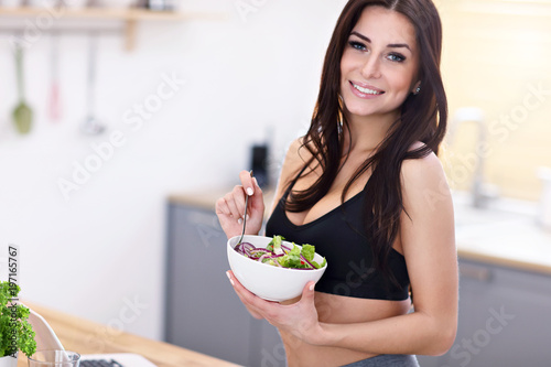 Fit smiling young woman with salad in modern kitchen