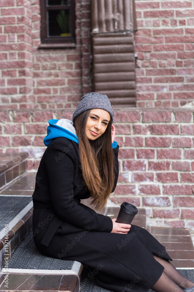 beautiful woman in black coat sitting with a coffee to go beautiful woman in black coat sitting with a coffee to go