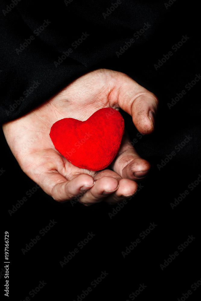Palm of a peasant woman with plush red heart on a black fabric. Palm of a peasant woman with plush red heart on a black fabric.
