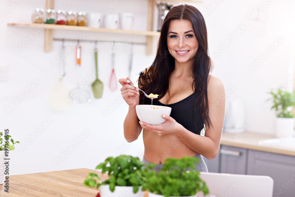 Fit smiling young woman with bowl of corn flakes in modern kitchen