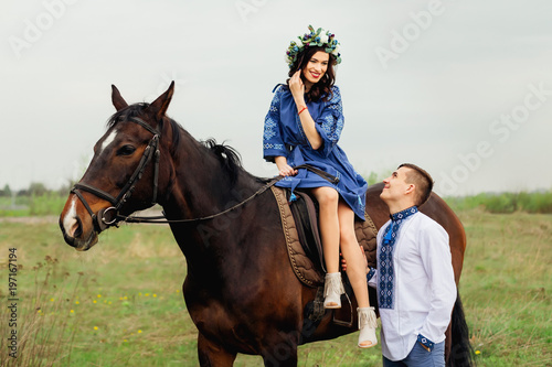 The charming smile of a girl who elegantly sits in a saddle on a horse and her boyfriend looks at her