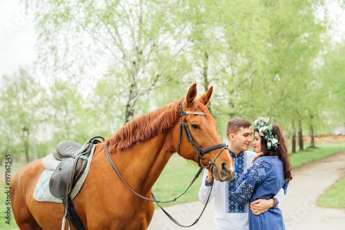 a handsome young man gently embraces the girl in a chic dress and holds a horse for a bridle © Ivan