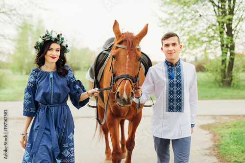 a couple in love in a festive blue clothes keeps a horse behind the bridle and looks at the camera lens