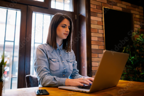 Smiling female copywriter working remote at laptop device connecting to wireless internet.Attractive female freelancer wit good mood chatting in social networks with friend sitting in coffee shop