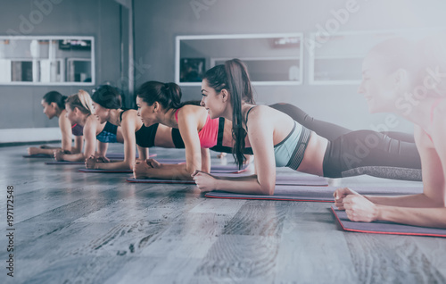 Happy group of young beautiful women in sportswear doing yoga exercises in plank position. Class of yoga or fitness