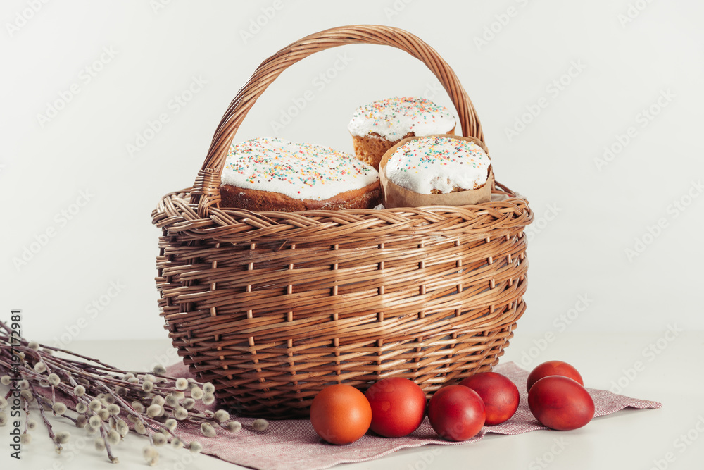 close-up view of basket with easter cakes, painted eggs and catkins on grey close-up view of basket with easter cakes, painted eggs and catkins on grey