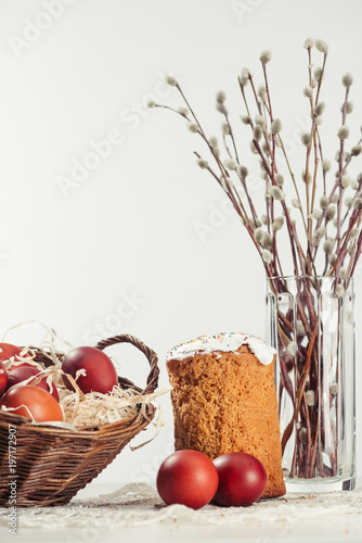 willow twigs in vase  easter cake and painted chicken eggs in basket on grey