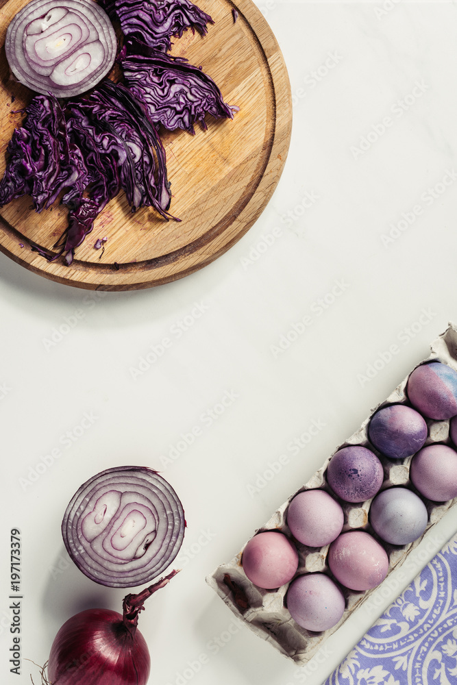 top view of painted easter eggs in egg box, purple cabbage and onions on grey