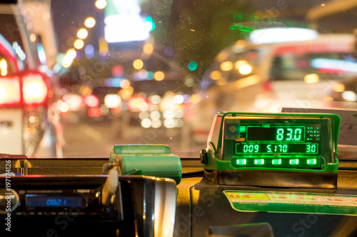 The digital taxi meter on the dashboard of cab shows kilometer and cost. Night taxi ride in traffic jam.