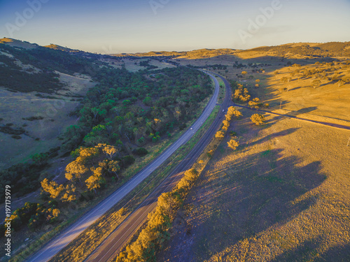 Aerial view of Hume Highway passing through beautiful countryside with long shadows from trees at sunset in Australia