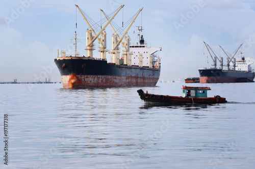 Small passenger boat running in the sea and have cargo ship.