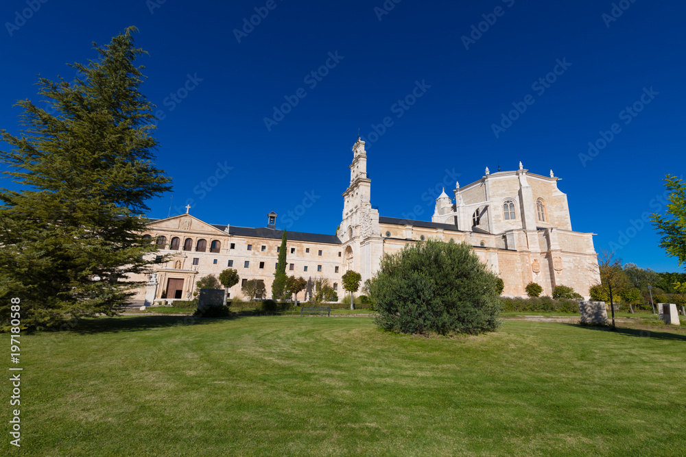 side view of Monastery Santa Maria de la Vid, with church, landmark and monument from twelfth century, with green grass and blue sky, in Burgos, Castile and Leon, Spain, Europe
