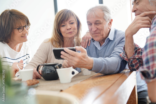 Group of senior friends looking at pictures on smartphone