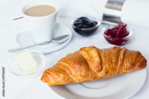 Croissant breakfast served with jams  butter and a cup of coffee with milk