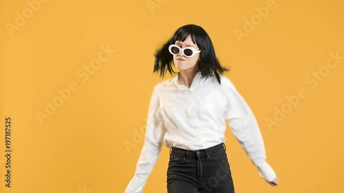 Portrait closeup of happy stylish female with bob hairdo wearing fancy sunglasses dancing energetic disco in 60's, over yellow background. Concept of emotions