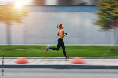 A beautiful sporty woman runing on street in sportswear. Training sun day. Big gray wall behind photo
