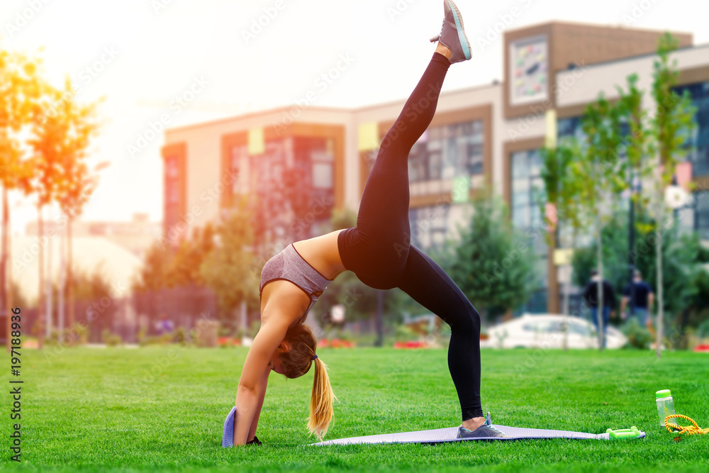 Fototapeta premium Yogi woman practicing yoga outdoor in the park, standing in bridge exercise, one legged wheel pose, wearing sportswear, full length, side view