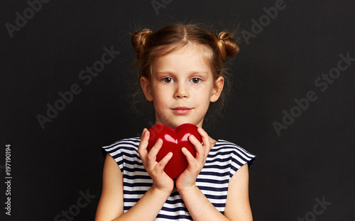 Adorable girl holding red heart over dark background. Concept of love, help and protection. 