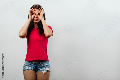 Young, beautiful girl makes binoculars out of hands, visionary. Isolated on a light background. Different human emotions, feelings of facial expression, attitude, perception, body language, reaction.