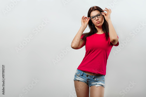 A young, beautiful girl adjusts her glasses. Isolated on a light background. Different human emotions, feelings of facial expression, attitude, perception, body language, reaction.