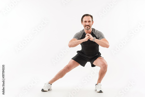 Horizontal photo of muscular man doing workout with stretching legs and sit-ups keeping hands in front of him, isolated over white background © Drobot Dean