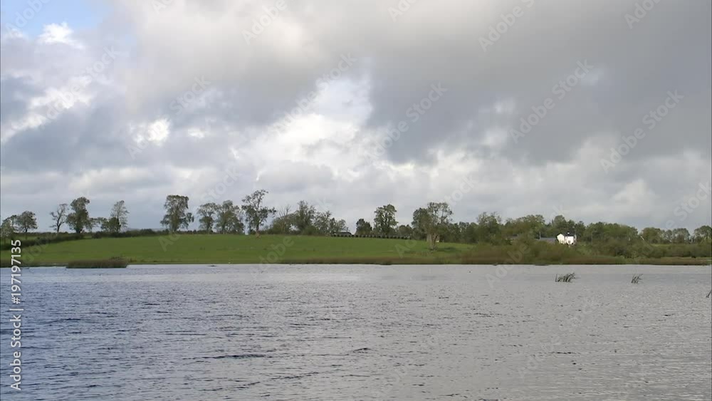 Still shot of a tranquil river with green hills covered in trees, under a blue cloudy sky. Still shot of a tranquil river with green hills covered in trees, under a blue cloudy sky.