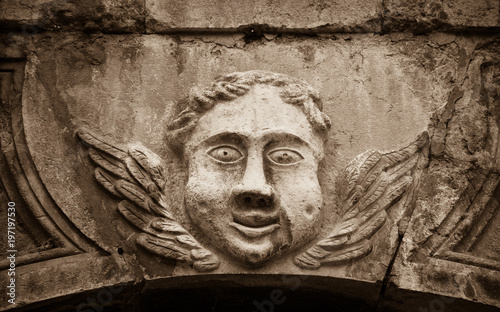 Smiling face of angel on the front of Cathedral of Notre Dame of Assumption in Entraveaux (Alpes de Haute Provence, France). Sepia photo.