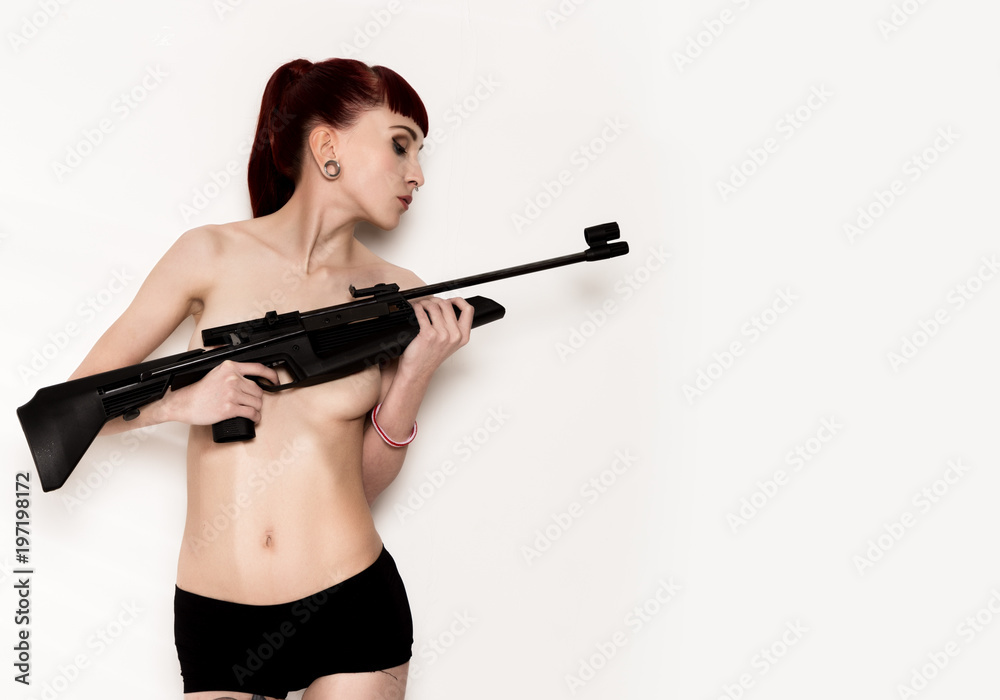 Beautiful sexy redhead holding pneumatic weapon on a light background. free space for your text Beautiful sexy redhead holding pneumatic weapon on a light background. free space for your text
