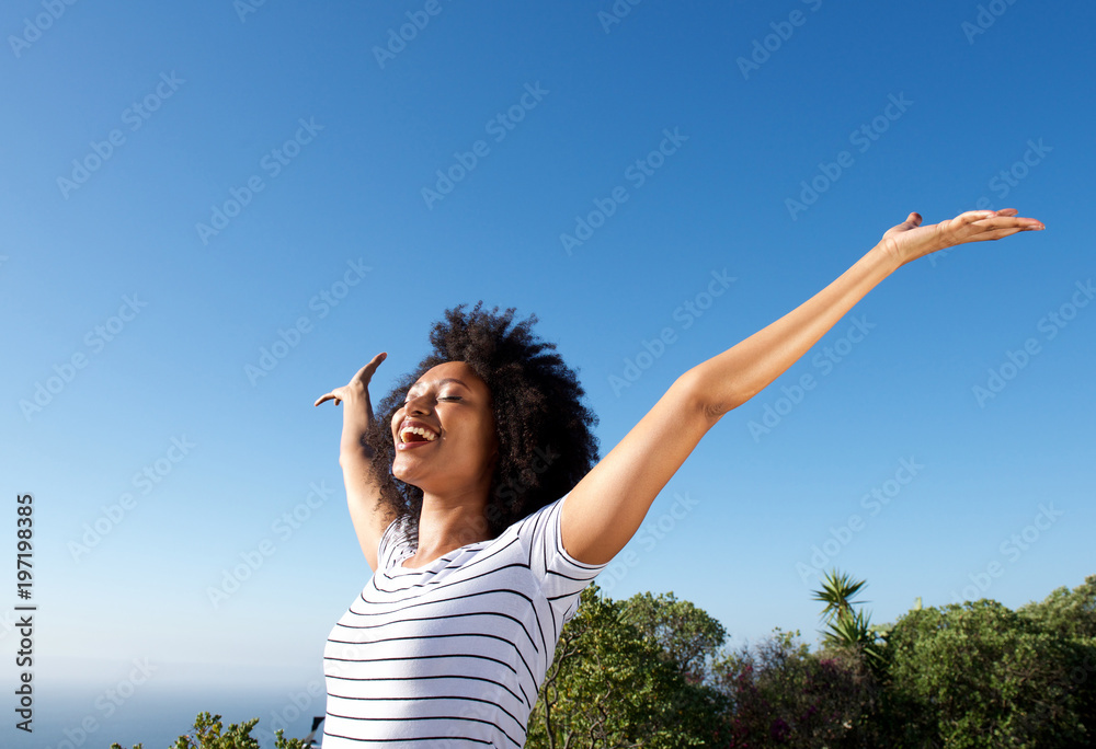 young african woman standing outdoors with arms raised and laughing