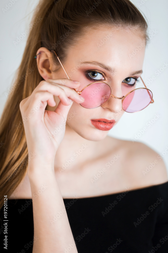 Sexy blonde woman in pink glasses on white background. Beautiful girl with professional makeup looking at the camera Sexy blonde woman in pink glasses on white background. Beautiful girl with professional makeup looking at the camera