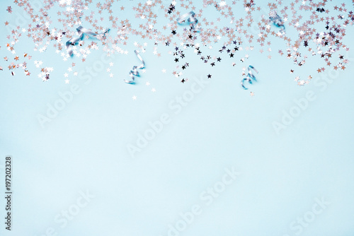 Star shaped silver sequins and silver ribbons over blue background. Copy space.