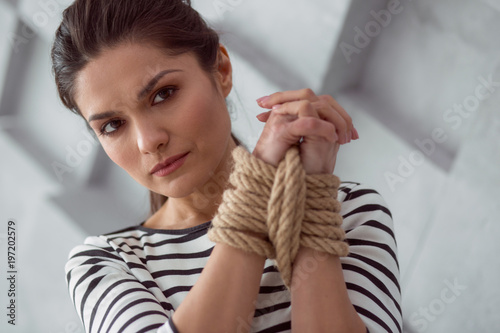 Female victim. Sad moody cheerless woman holding her hands together and looking at you while being tied up