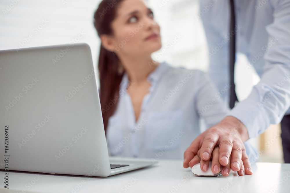 Sexual abuse. Nice pleasant young woman sitting at the table and working while feeling a male hand on hers Sexual abuse. Nice pleasant young woman sitting at the table and working while feeling a male hand on hers
