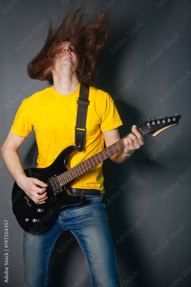 Obraz premium Man with long hair in yellow t-shirt, playing on electric guitar rock. Fashion studio portrait on a gray background.