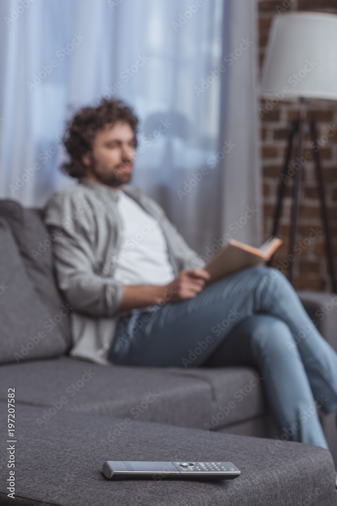 handsome man holding book with remote control on foreground handsome man holding book with remote control on foreground