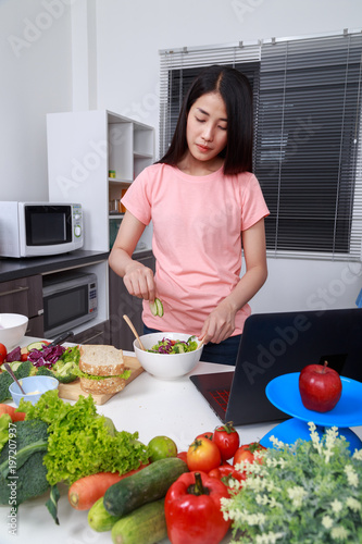 woman mixing salad while cooking with laptop in kitchen