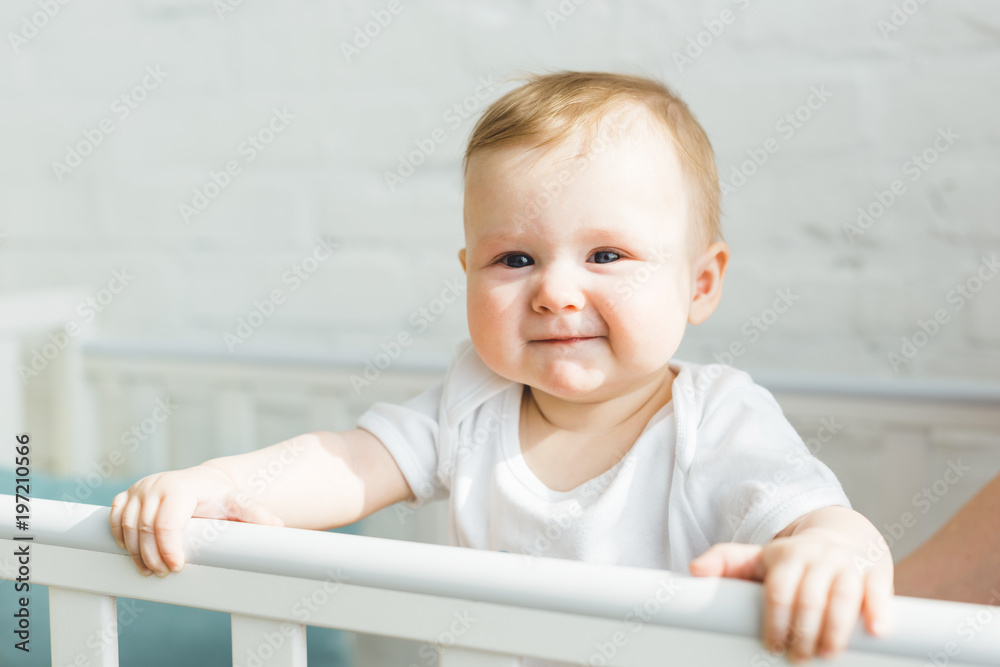 Cute smiling infant standing in crib